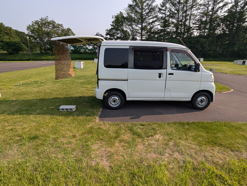 オートキャンプ場内の駐車スペースに止めているダイハツ ハイゼットカーゴ。車中泊仕様に変更