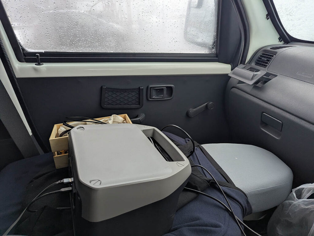 車内の助手席に置かれたポータブル電源と木箱、曇った窓の向こうは雪景色