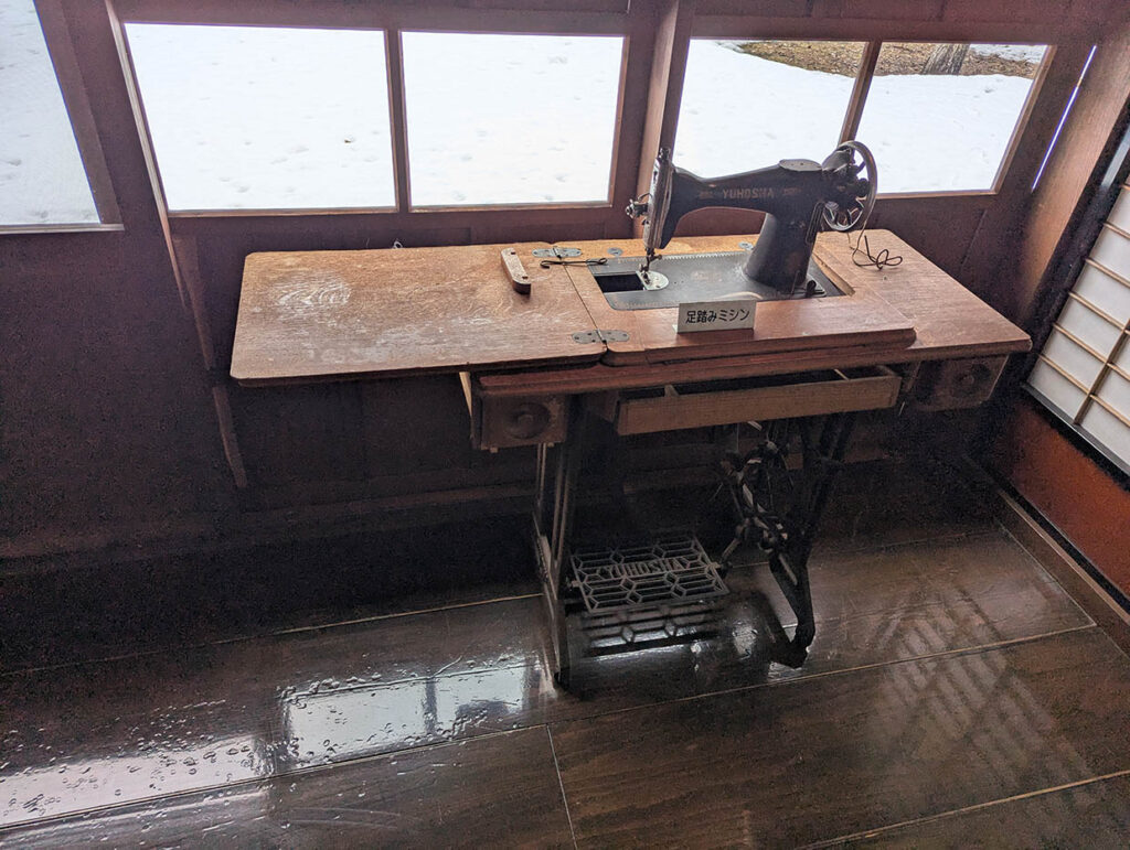 木製の机に設置された古い足踏みミシン。窓の外には雪が残る。