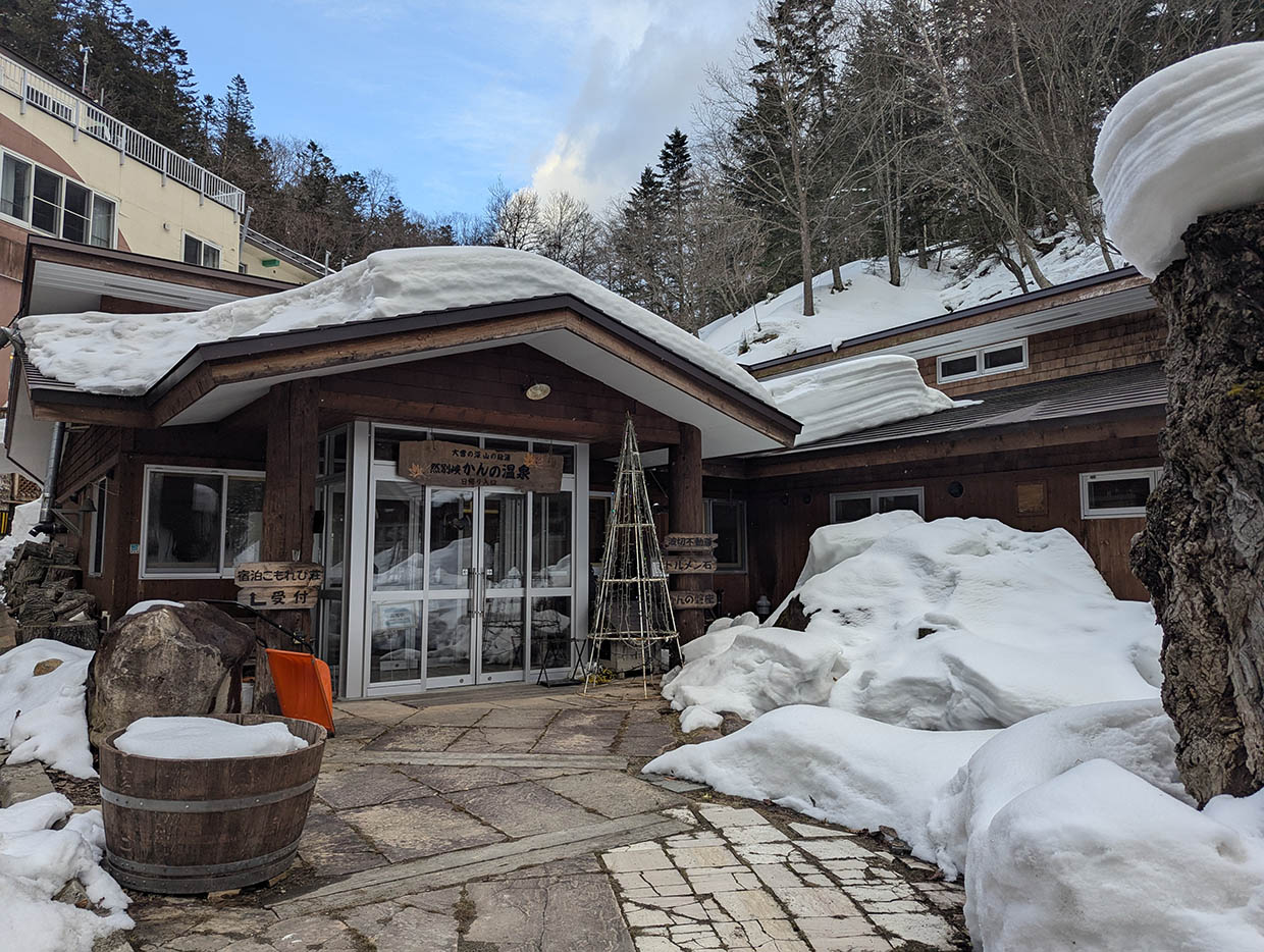 冬の雪に包まれた山間の温泉宿「然別峡かんの温泉」の外観。木造の建物と雪のコントラストが美しい。