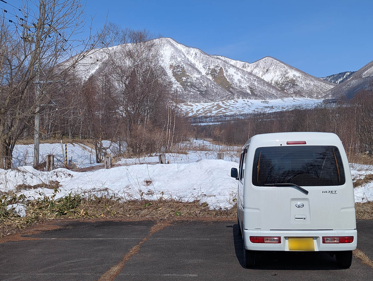 雪景色のヌプカの里駐車場に停めた白いハイゼットカーゴと、遠くに広がる青空と山並み