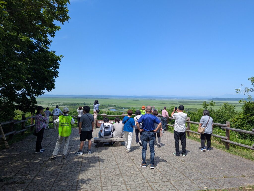 細岡展望台の展望スペースから見える釧路湿原の広大な景色と、空を見上げる観光客たち