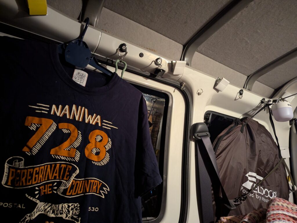 車中泊の車内に吊るされたNANIWA728のTシャツと荷物