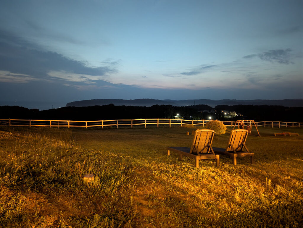 夜の庭に置かれたリクライニングチェア。遠くの町の明かりと海が見える