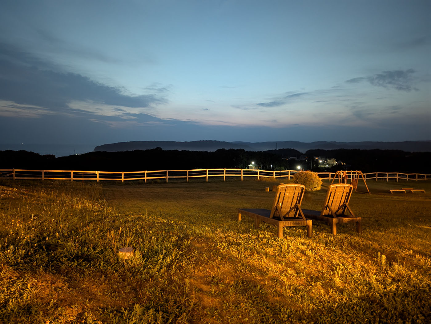 夜の庭に置かれたリクライニングチェア。遠くの町の明かりと海が見える