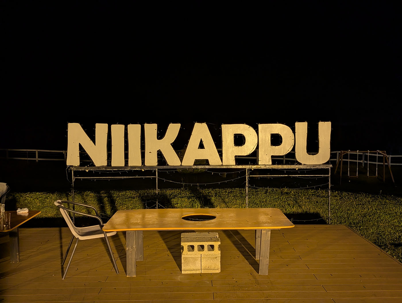 夜のテラスに置かれた「NIIKAPPU」のライトアップされたサインとテーブル