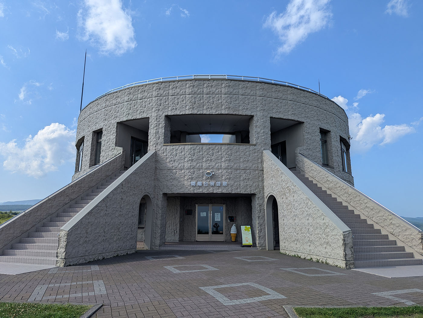 開陽台展望館の正面全景。青空の下、円形の建物から左右に伸びる階段が特徴的。