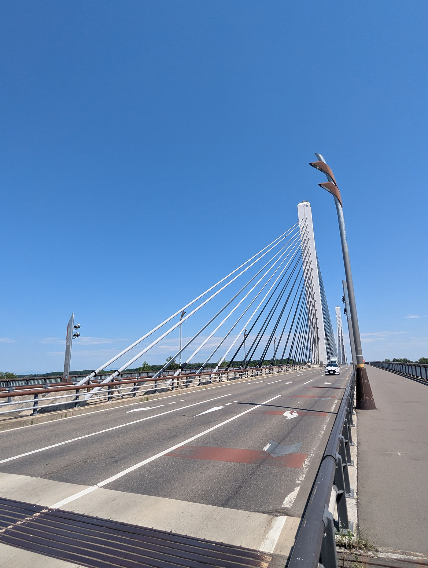 快晴の青空の下、十勝大橋の斜張橋が一直線に延びる。道路の白線とケーブルが奥行きを強調している。