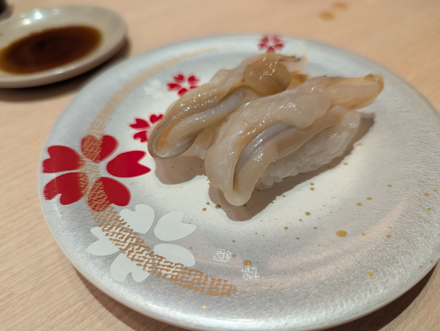 帯広の回転寿司「魚まる」で注文した貝の握り寿司。白い皿に2貫盛られ、奥には醤油皿が見える。