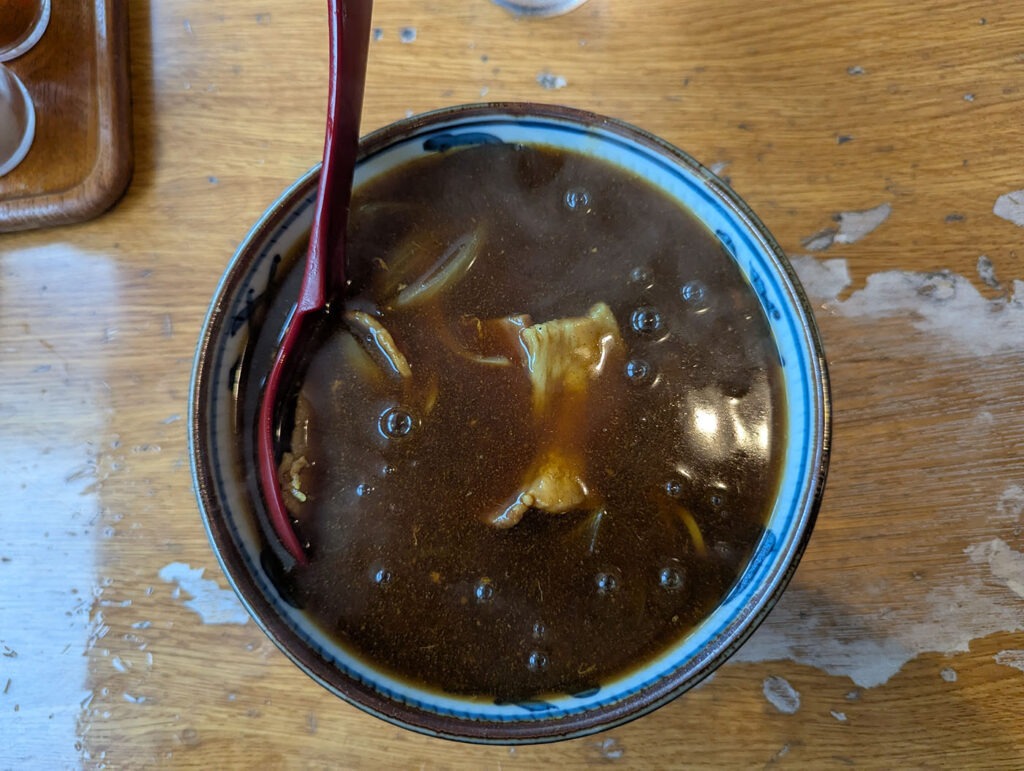 いブラウンのカレーあんがたっぷりかかった、夕張・栗下食堂名物のカレーそば。湯気が立ちのぼり、赤いレンゲと器の縁が食欲をそそる。
