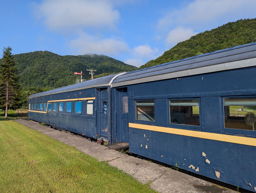 富内銀河ステーションに保存された青い客車。外装の塗装はところどころ剥がれているが、山並みと青空を背景に当時の姿を静かに伝えている。