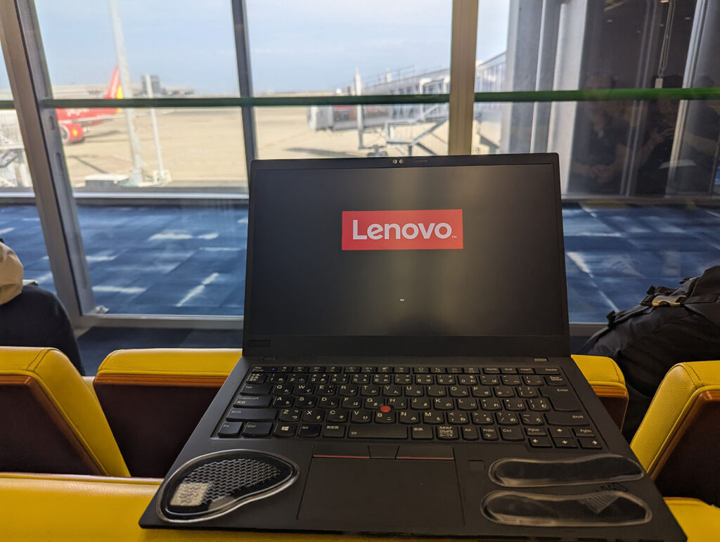 空港の搭乗口付近で開かれたLenovoノートパソコン。窓の外には飛行機が見える。