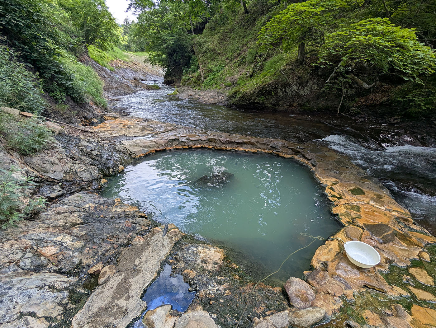 川沿いに湧く然別峡・鹿の湯温泉。石で囲まれた湯船が自然の中に溶け込むように佇み、交互浴も楽しめる秘湯。