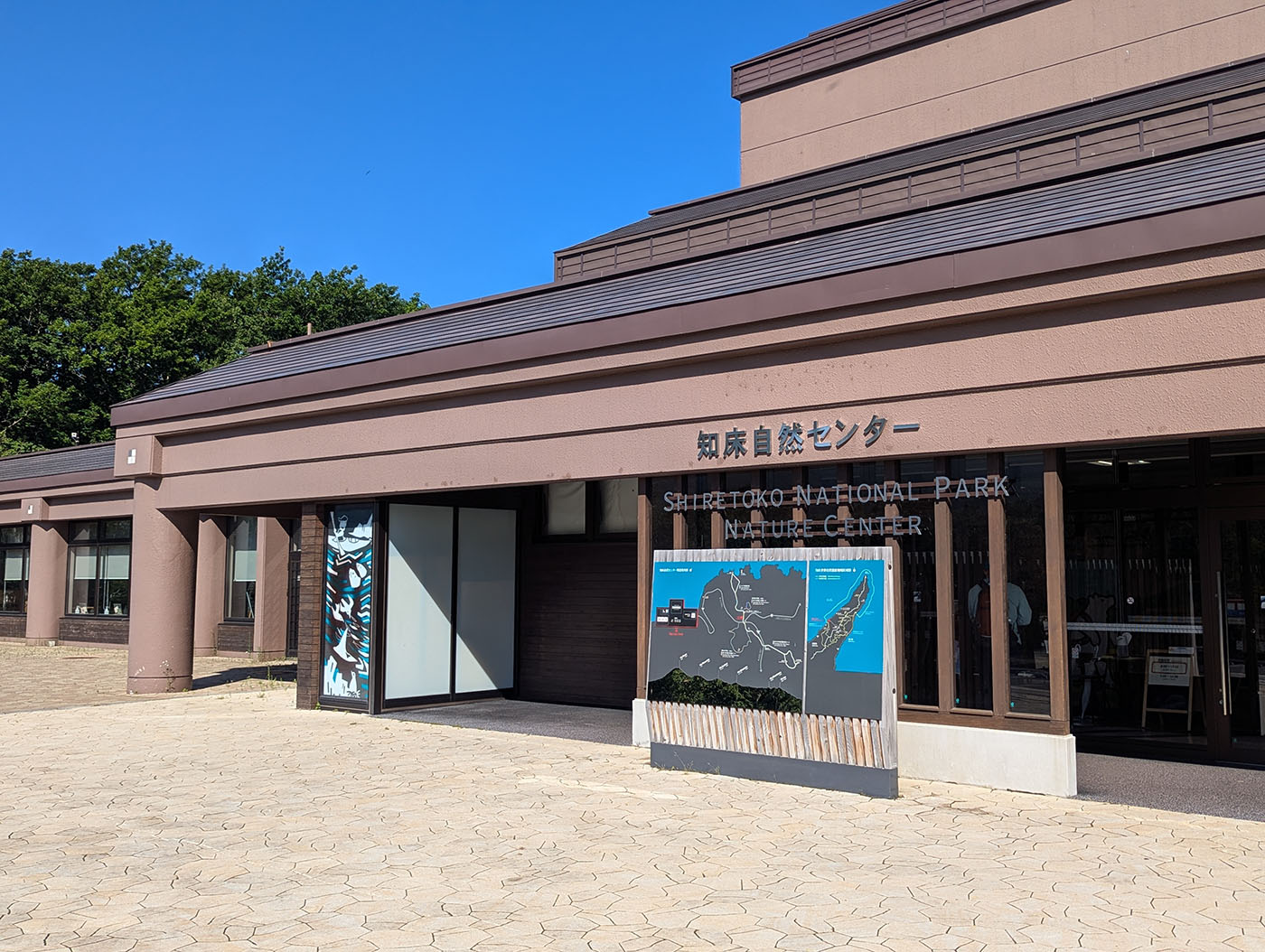 青空の下に建つ知床自然センターの外観。入口横には知床半島の地図看板が設置されている。