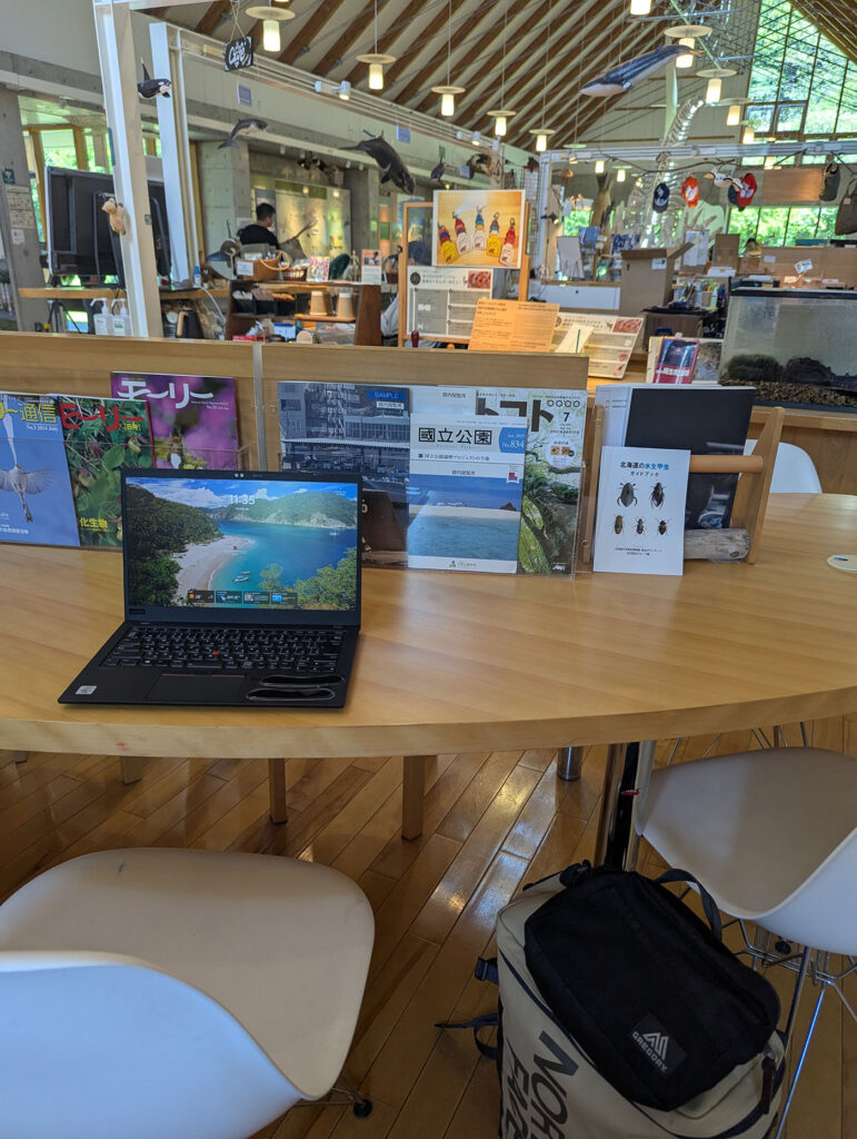 知床羅臼ビジターセンター館内のテーブル席。観光情報冊子や雑誌が並び、奥には展示スペースが広がる。