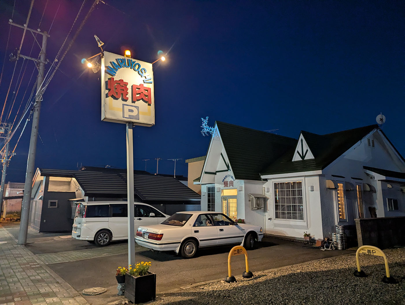 夜の街に佇む「焼肉まるよし」の外観と看板。ライトアップされた看板と温かい灯りが、訪れる人を迎えている。