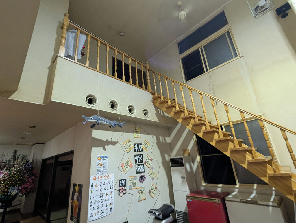 びっくり寿司の店内。木製の階段と昭和感あふれる内装、天井には扇風機、壁にはチョウザメ推しのポスターや飾りが並ぶ。