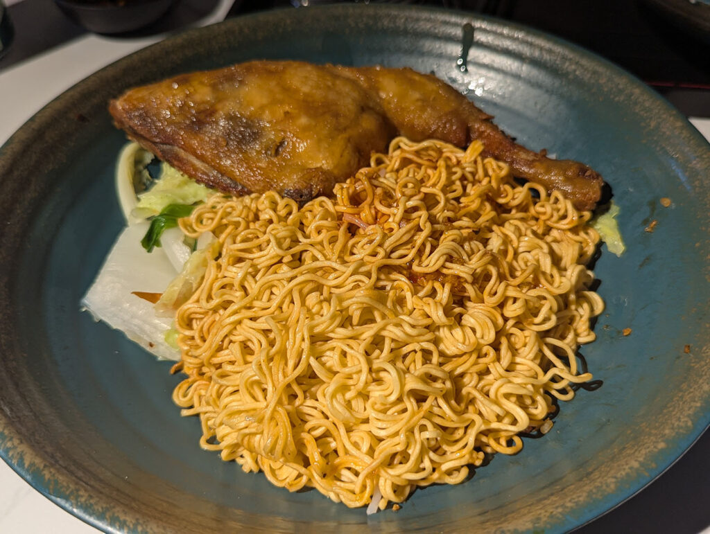 大きなチキンレッグとインスタント麺風の炒め麺が盛られた一皿。シンプルだがボリューム満点の料理。