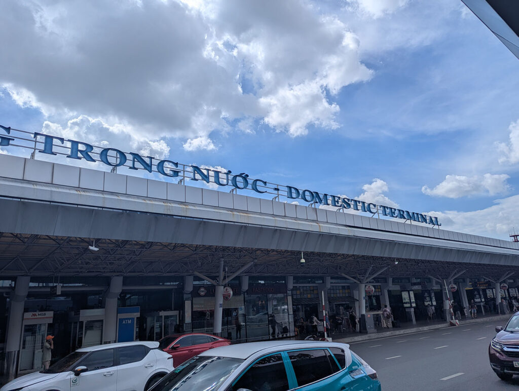 ホーチミン・タンソンニャット国際空港の国内線ターミナル前。青空の下、建物の屋根に「DOMESTIC TERMINAL」の文字が掲げられている。