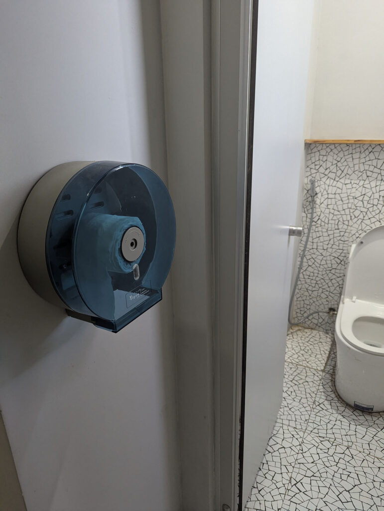 トイレの外側の壁に、大きな青いケースに入ったトイレットペーパーが設置されている。
