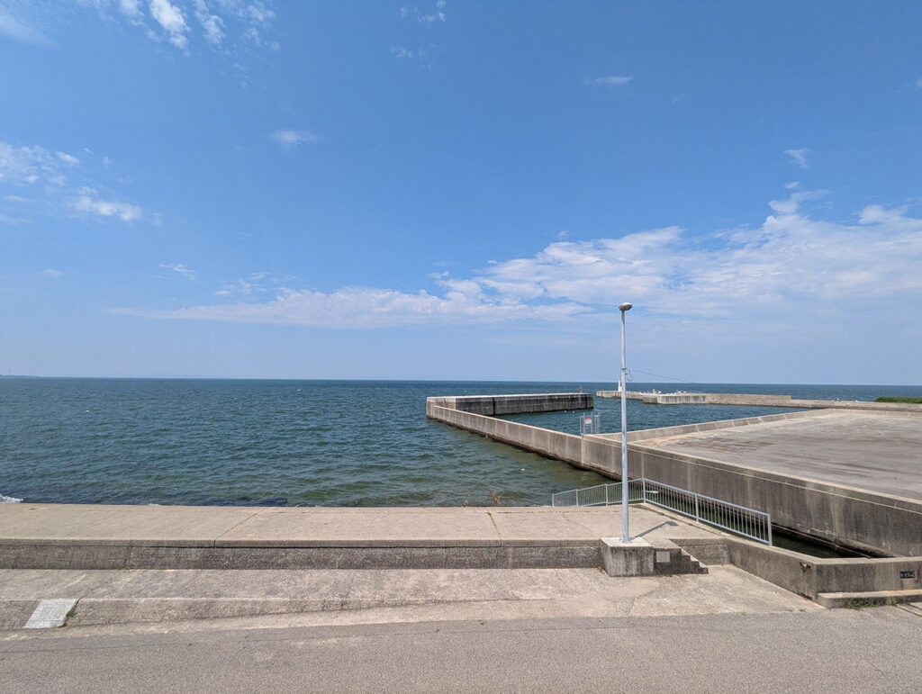 道の駅ウェーブパークなめりかわから見える富山湾の防波堤と港。コンクリートの岸壁が海に突き出し、青い海が水平線まで続く。夏の空には白い雲が浮かぶ。