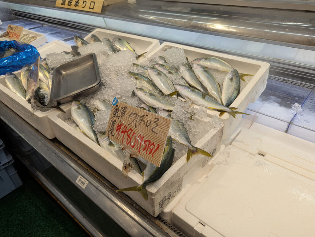 スーパー・バローの鮮魚コーナーに並ぶ新鮮なツバス(ブリの若魚)。氷の上で光る魚がずらりと並び、地元の海の恵みを感じさせる光景。