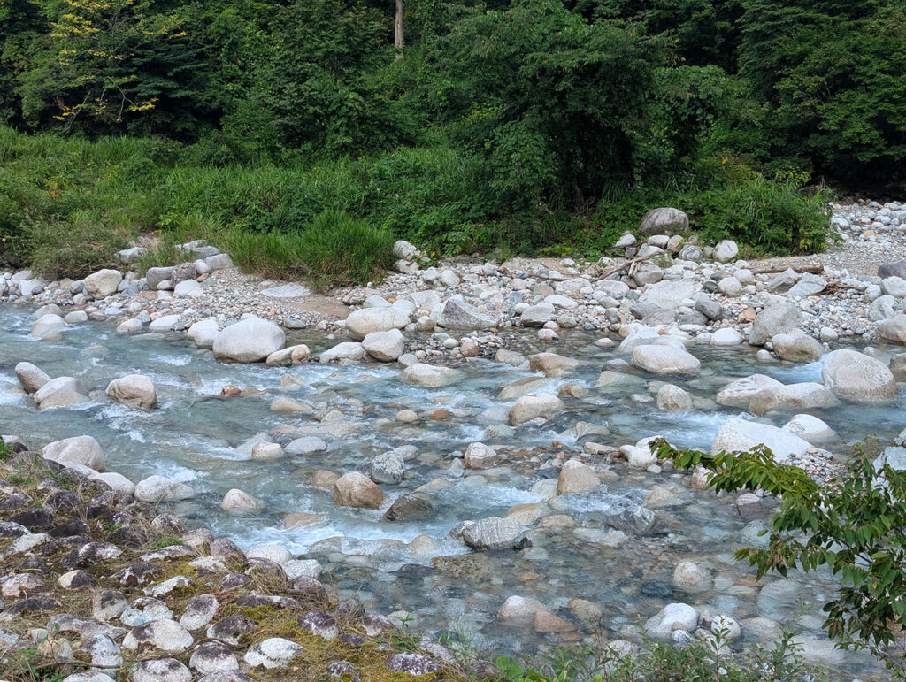 片貝山ノ守キャンプ場のそばを流れる清流。透明度の高い水が白い岩の間を流れ、周囲の緑が映り込む静かな山あいの川の風景。