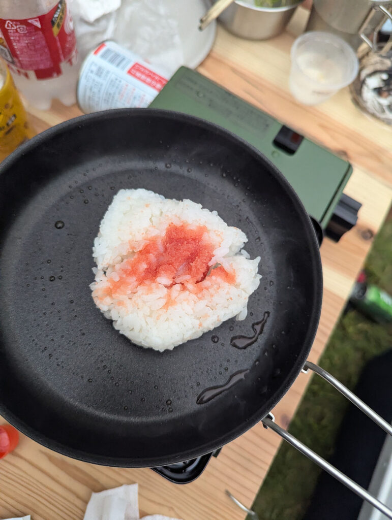 キャンプ用フライパンの上で焼かれる明太おにぎり。油がじゅっと弾け、香ばしい香りが広がる瞬間。